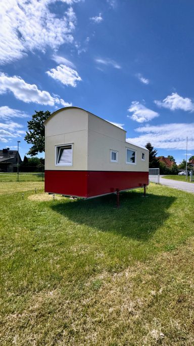 Das Tiny House "Red One" steht auf einer Wiese im Sonnenschein.